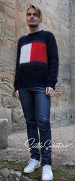 Men's black Tommy Hilfiger mohair crewneck sweater with large flag logo across chest, paired with dark jeans and white sneakers.