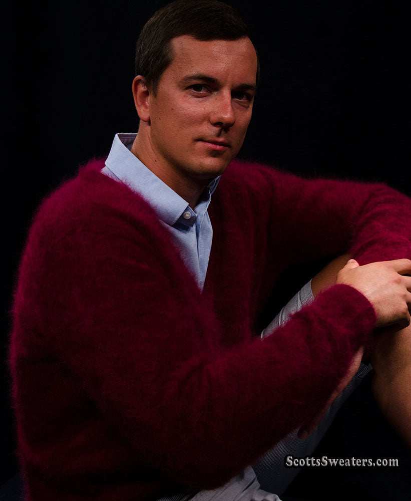 Man wearing a burgundy men's ultra-soft angora cardigan sweater over a light blue shirt against a dark background