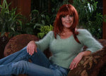 Woman wearing a light green fuzzy angora cropped 3/4-sleeve sweater with V-neck and blue jeans sitting on a patterned chair.
