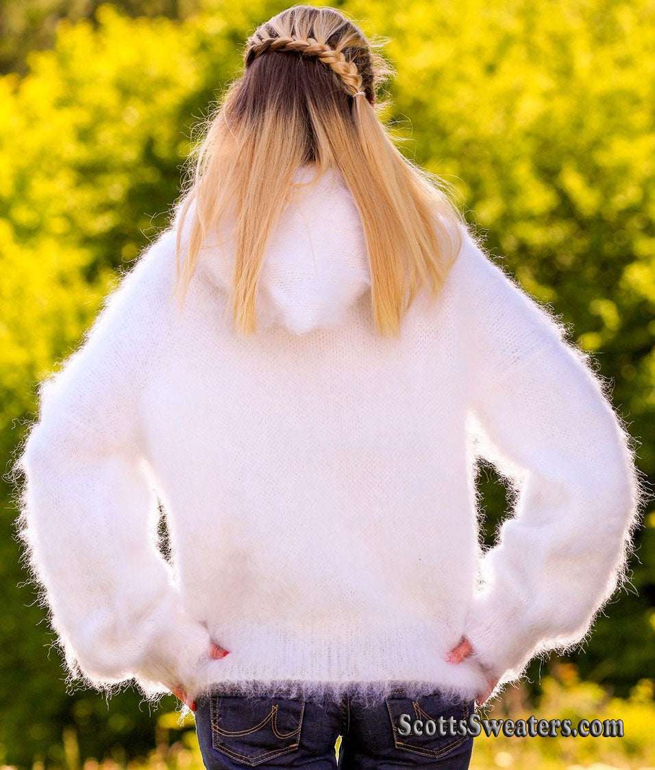 Woman wearing a white hand-knit mohair sweater jacket with hood from the back outdoors